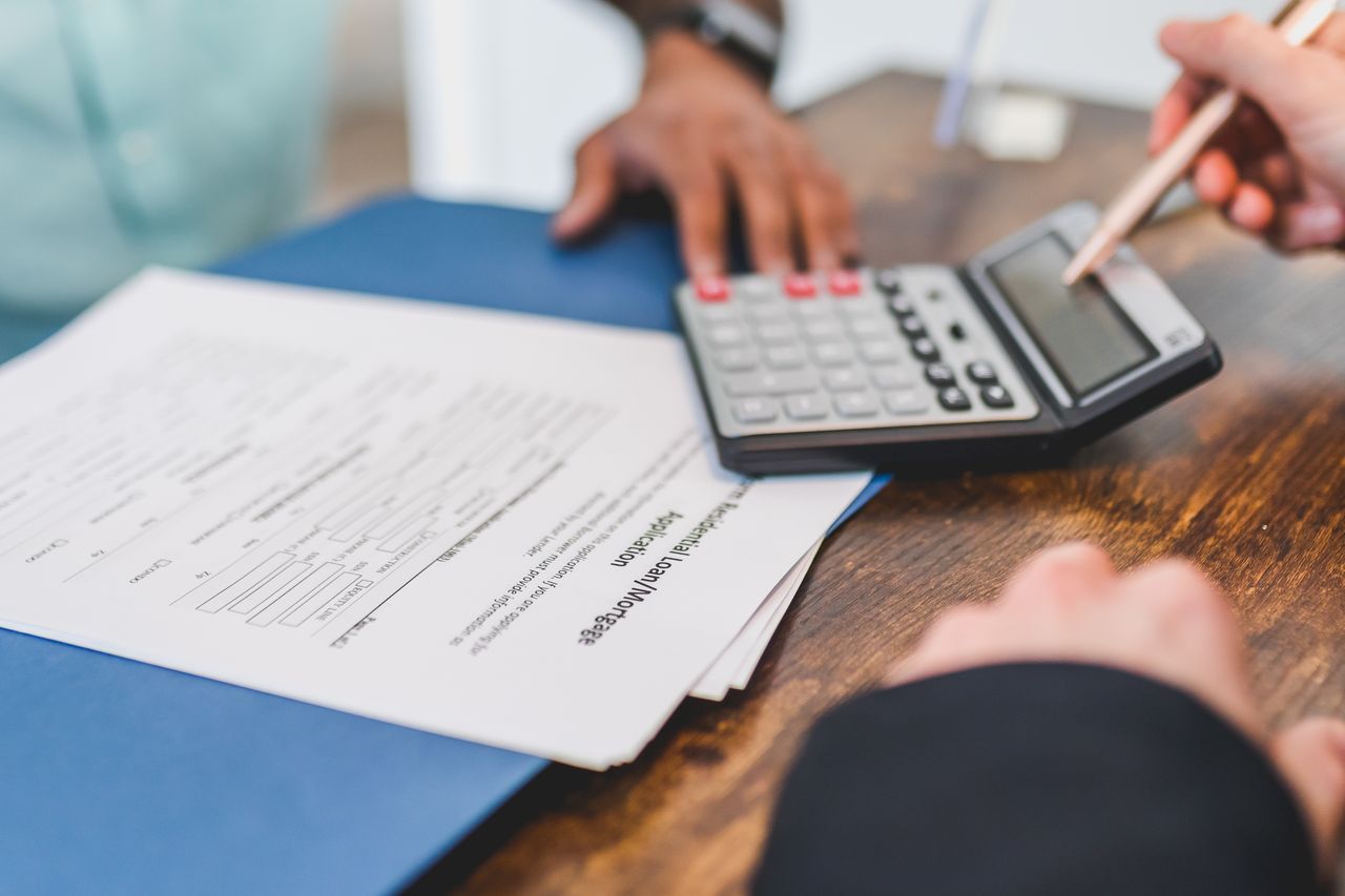 about-me-01 Hands using a calculator with real estate documents on a desk, indicating a financial transaction or meeting.